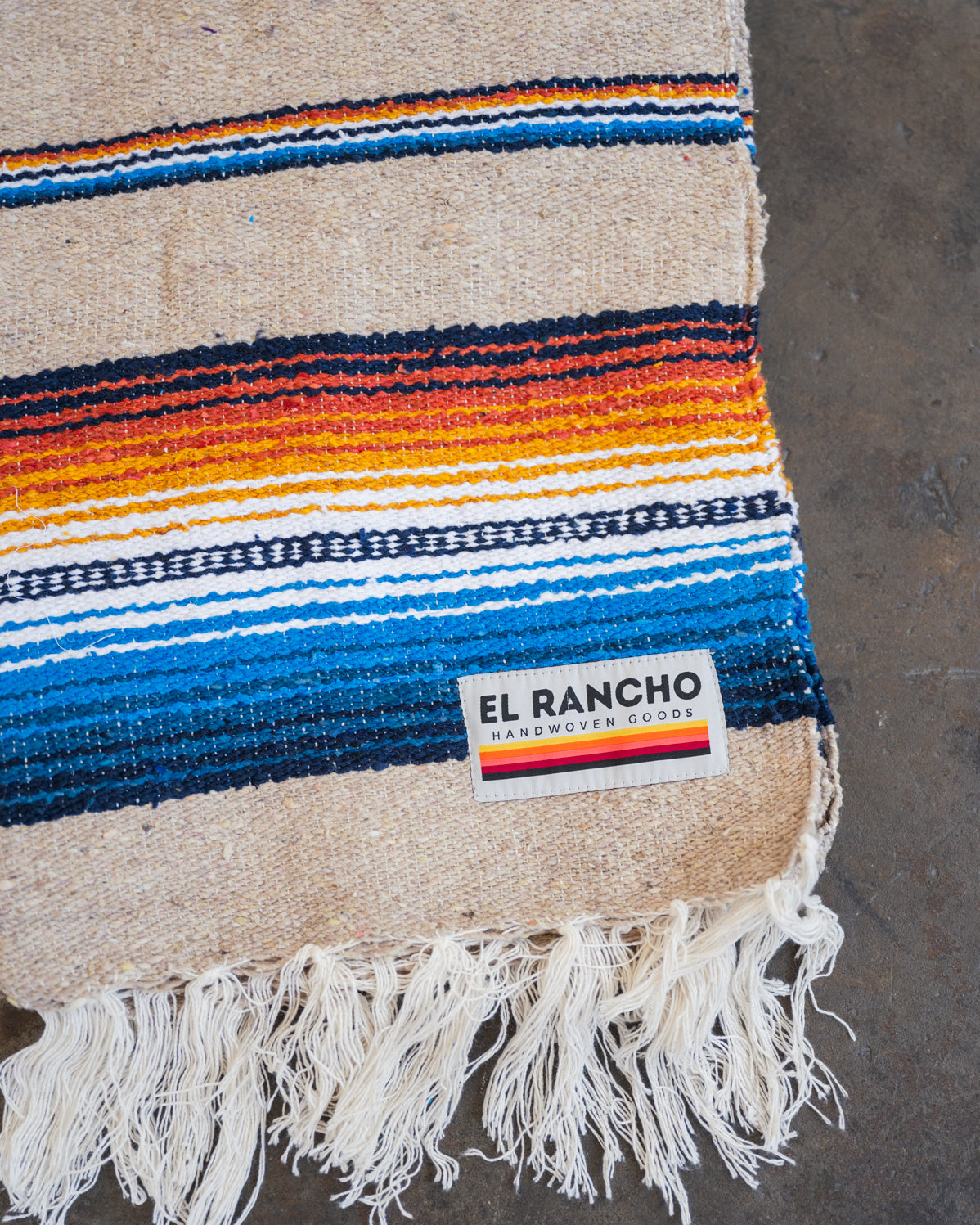 Multicolored Handwoven Saltillo Blanket laying on concrete floor folded in half