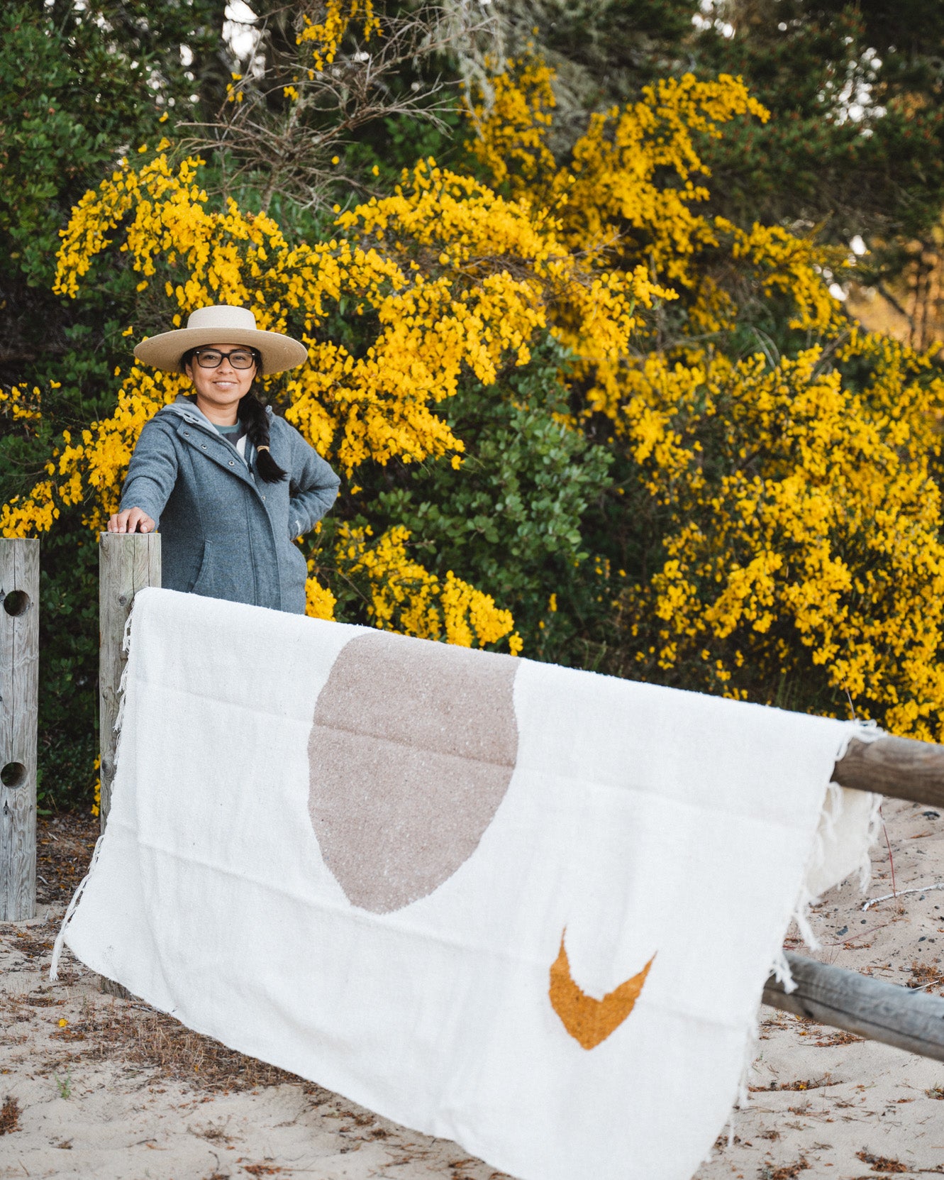 Woman standing next to cream blanket in front of yellow flowers.