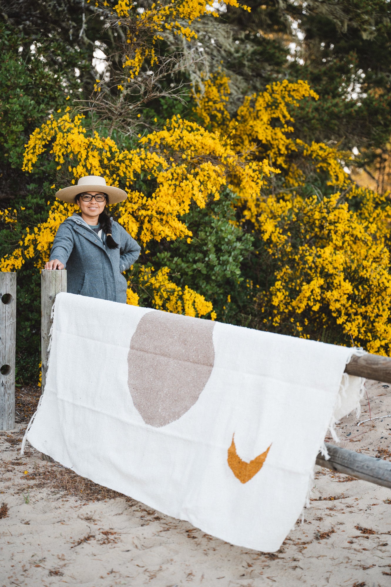 Woman standing next to cream blanket in front of yellow flowers.