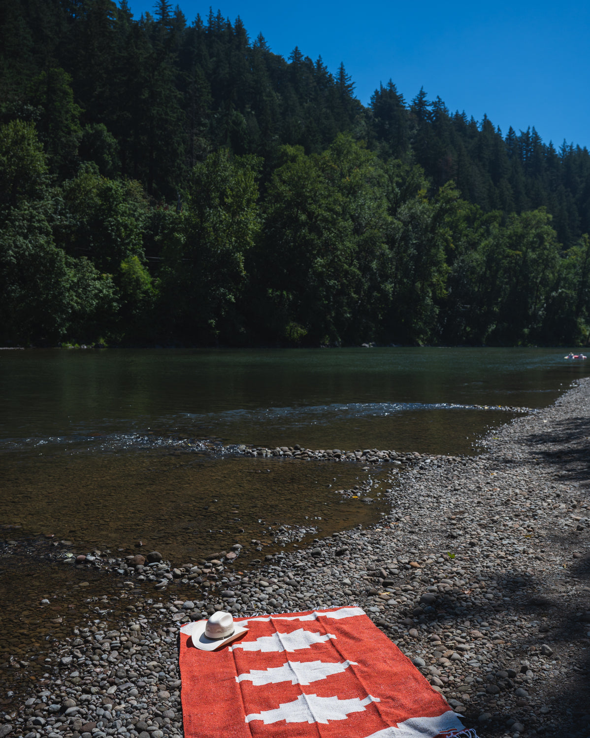 Red and white handowoven mexican blanket laying on a rocky riverbank