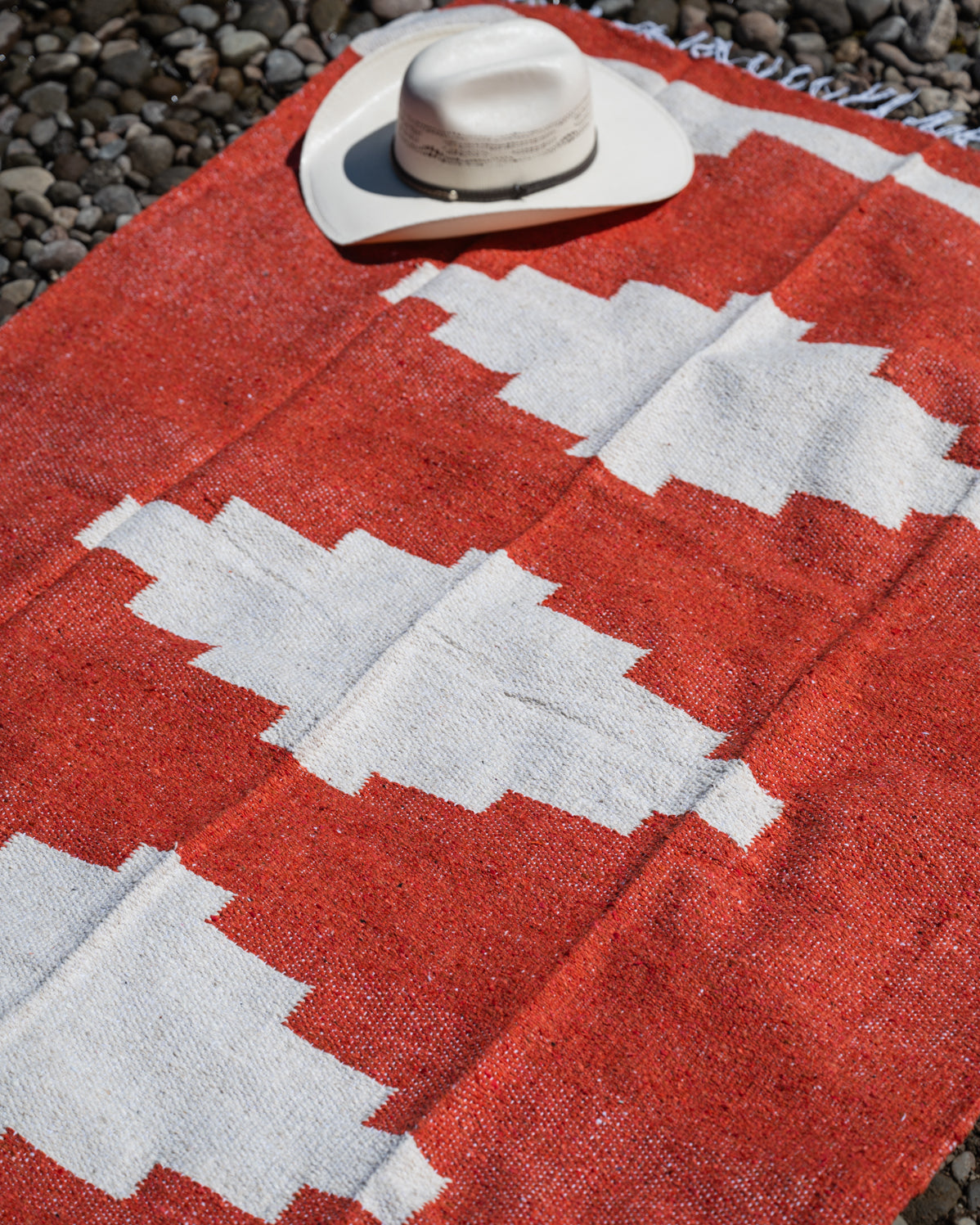 Red and white handowoven mexican blanket laying on a rocky riverbank