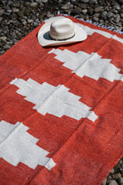 Red and white handowoven mexican blanket laying on a rocky riverbank