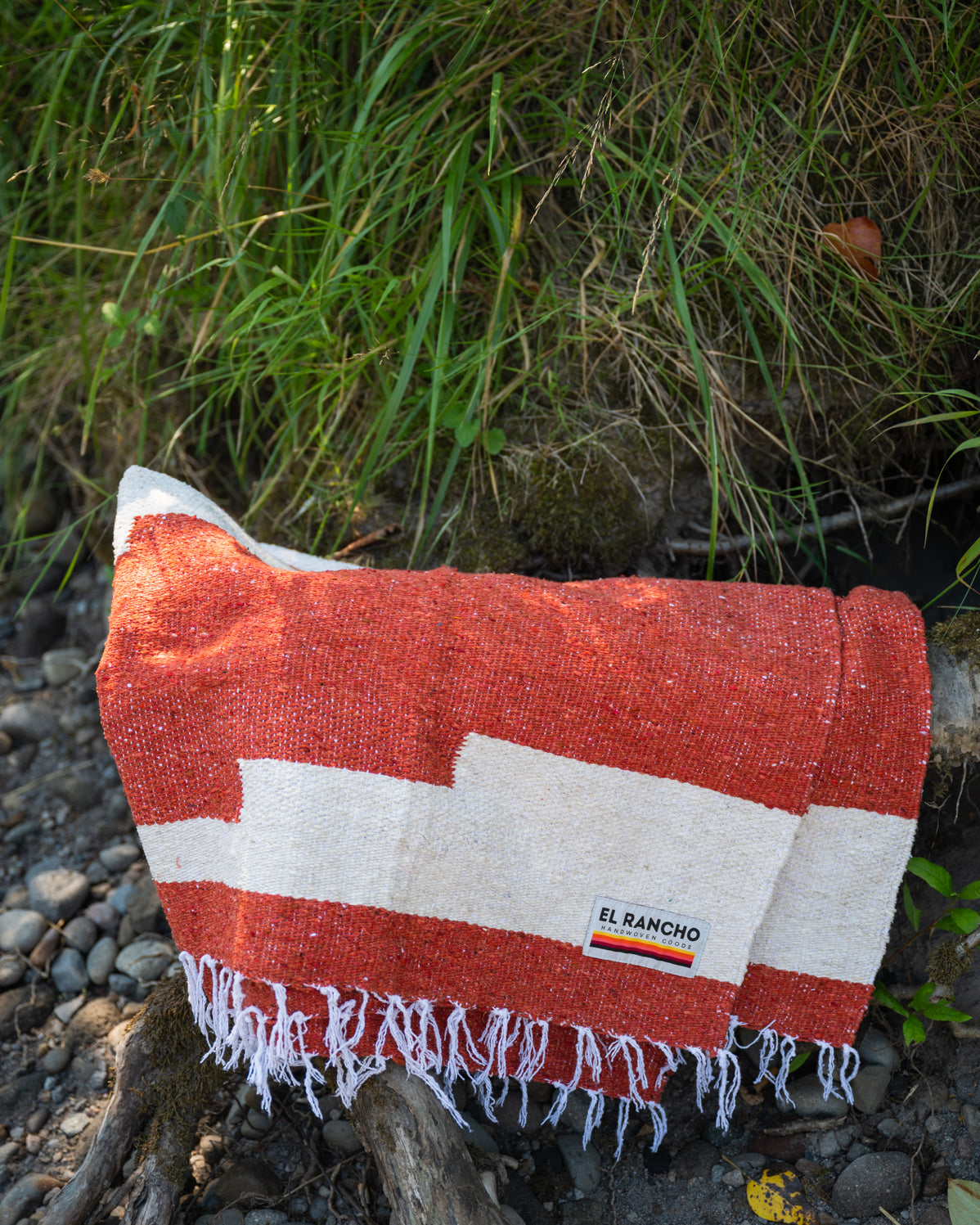 Red and white handowoven mexican blanket laying on a rocky riverbank