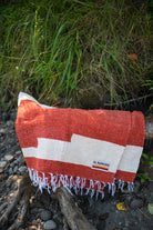 Red and white handowoven mexican blanket laying on a rocky riverbank