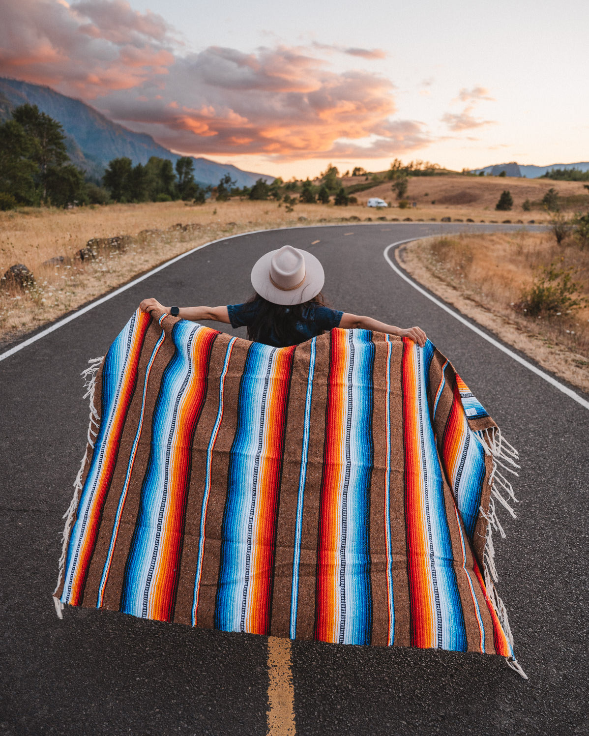 Woman walking down road holding handowoven saltillo blanket behind her at sunset