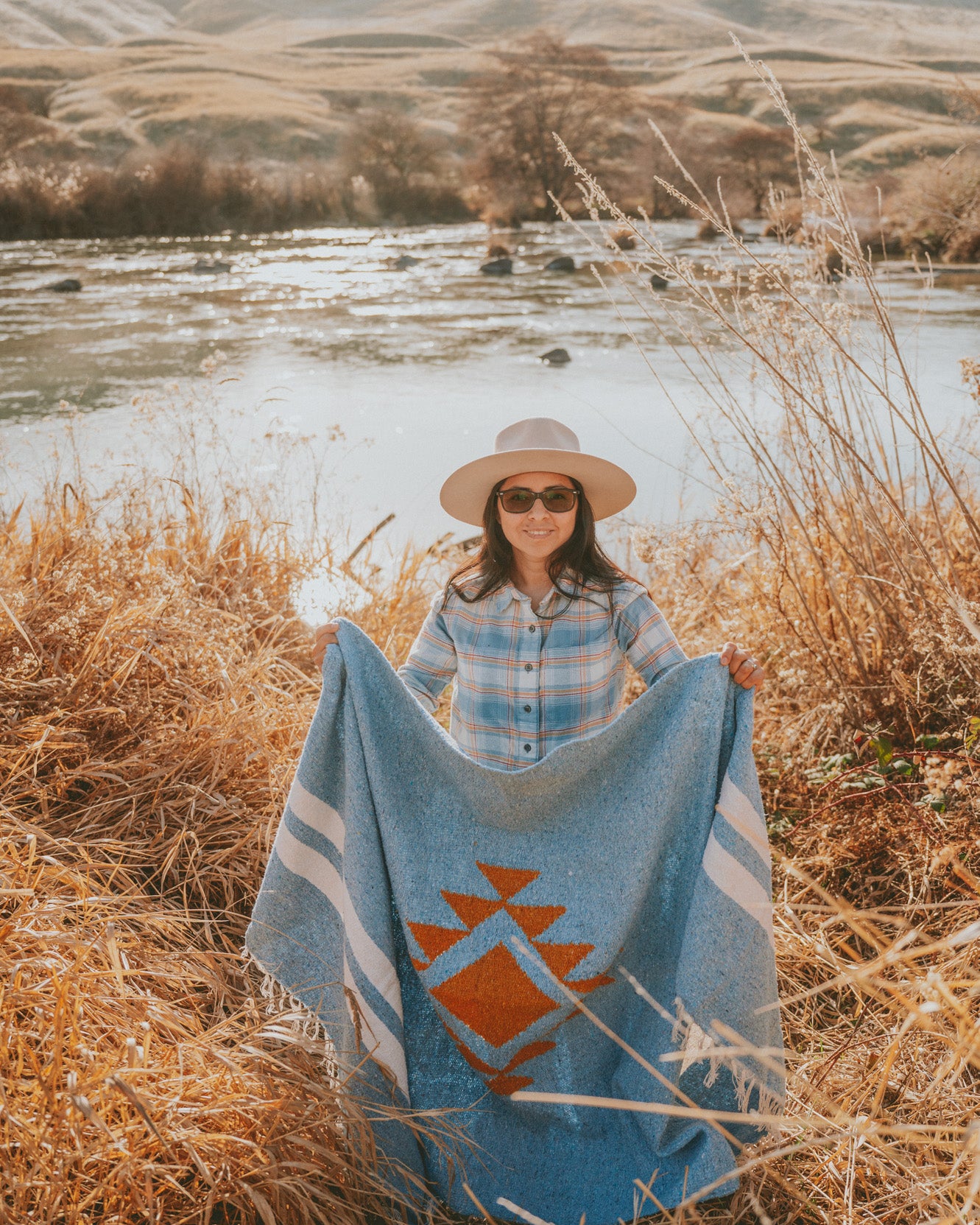 woman holding blue handwoven blanket in the high desert by a river