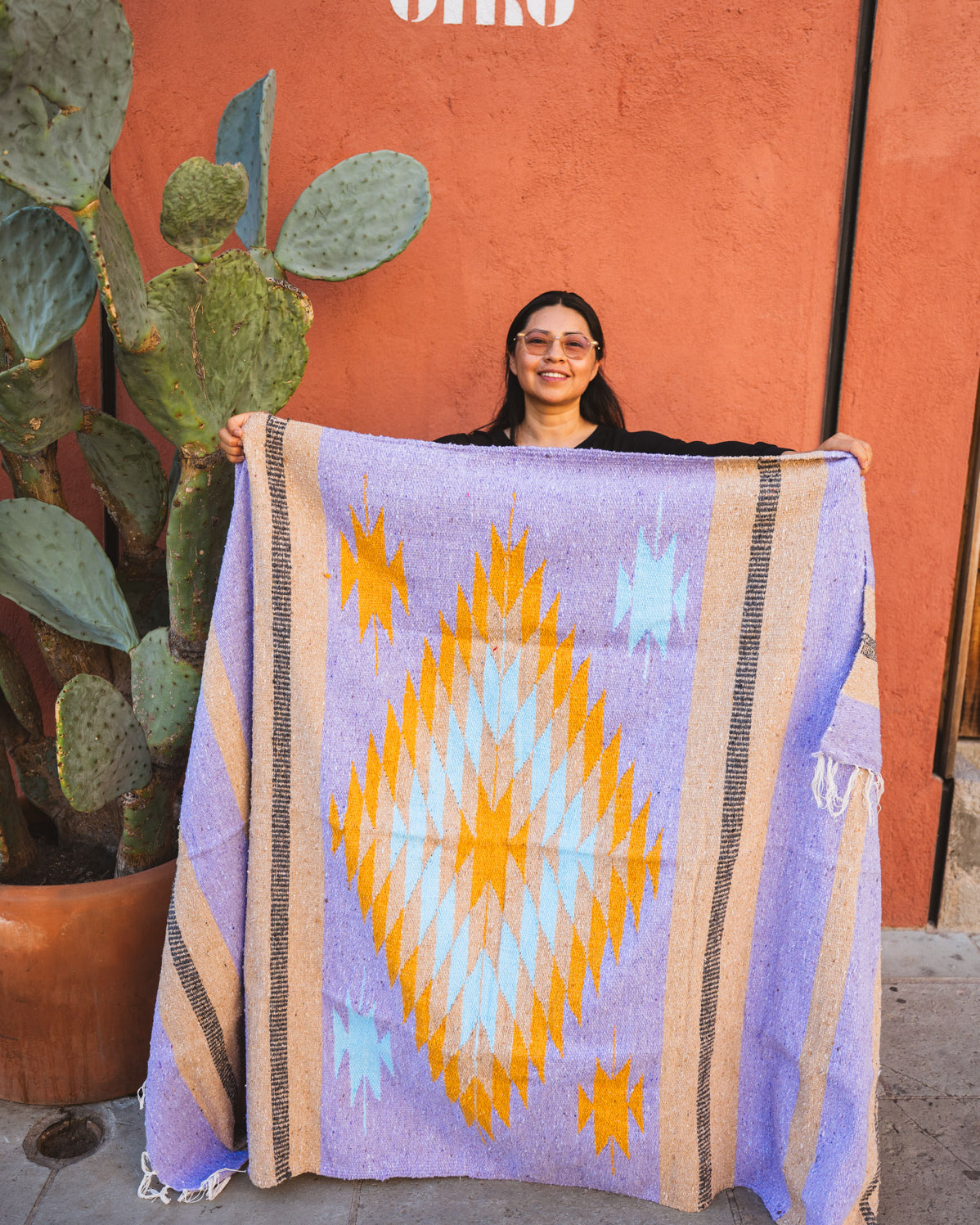 Person holding a colorful blanket with a geometric pattern against an orange wall.