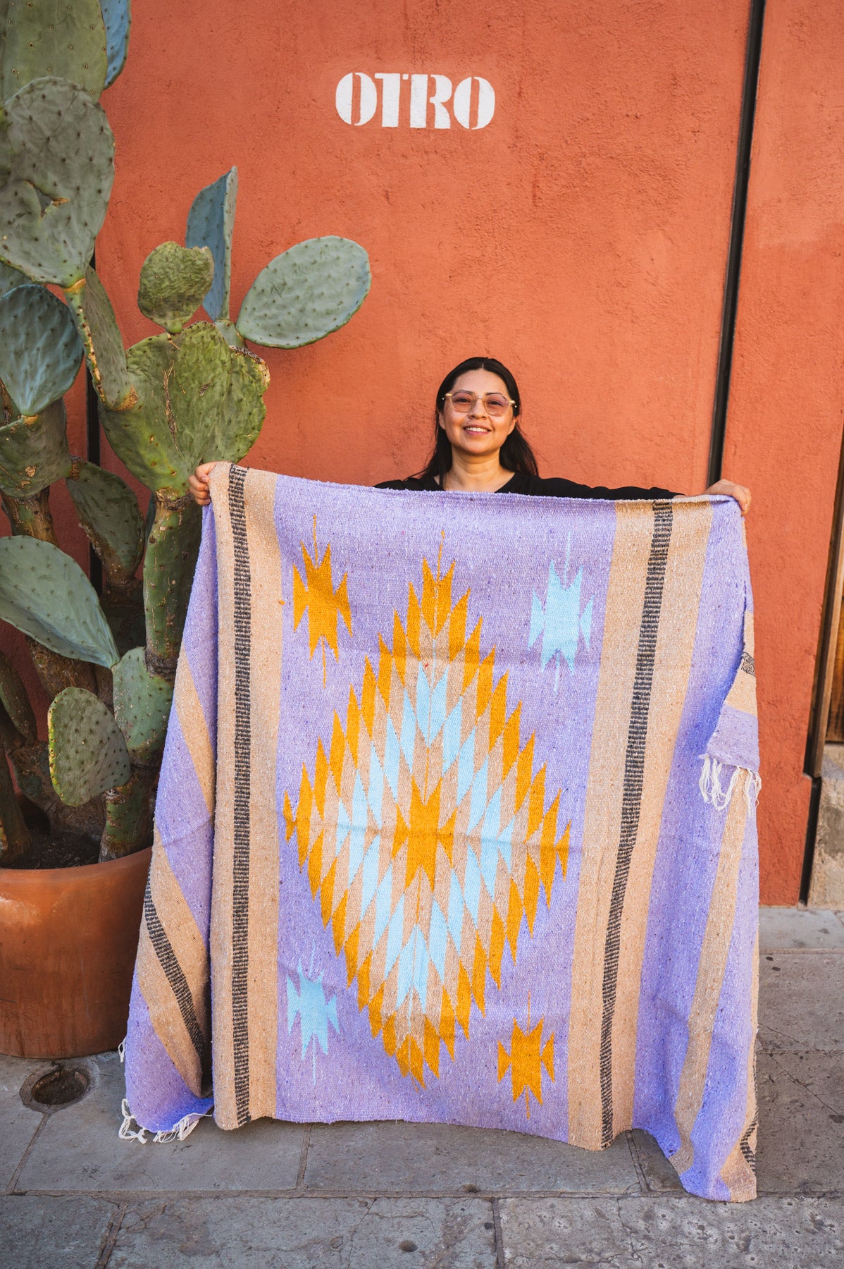 Person holding a colorful blanket with a geometric pattern against an orange wall.