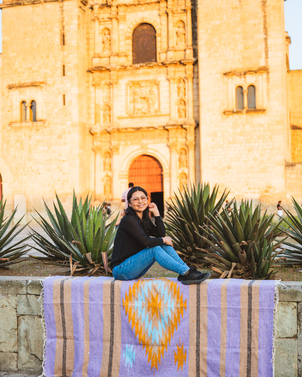 Santo Domingo Oaxaca and a girl sitting on a handwoven mexican blanket in front of it