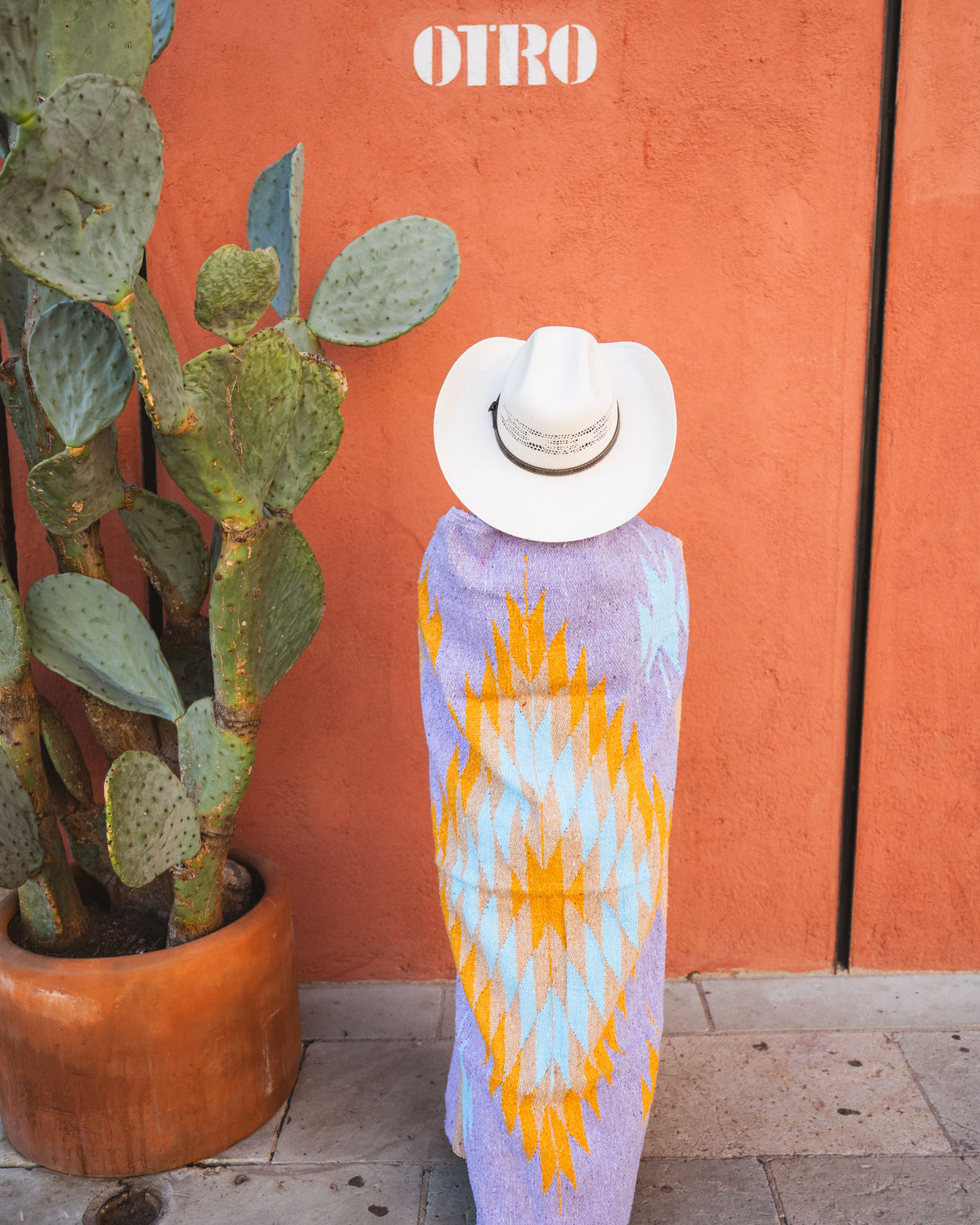 Girl wrapped in lavender handwoven mexican blanket in front of orange wall next to catctus