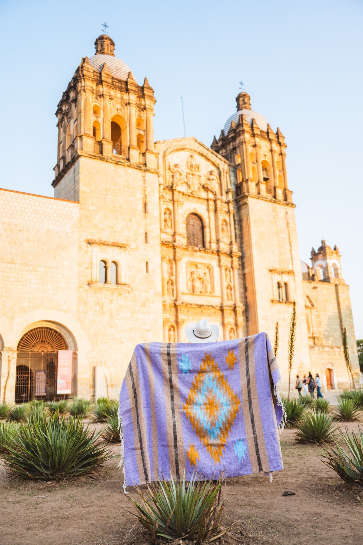 Santo Domingo Church Oaxaca and a girl standing with a handwoven mexican blanket in front of it