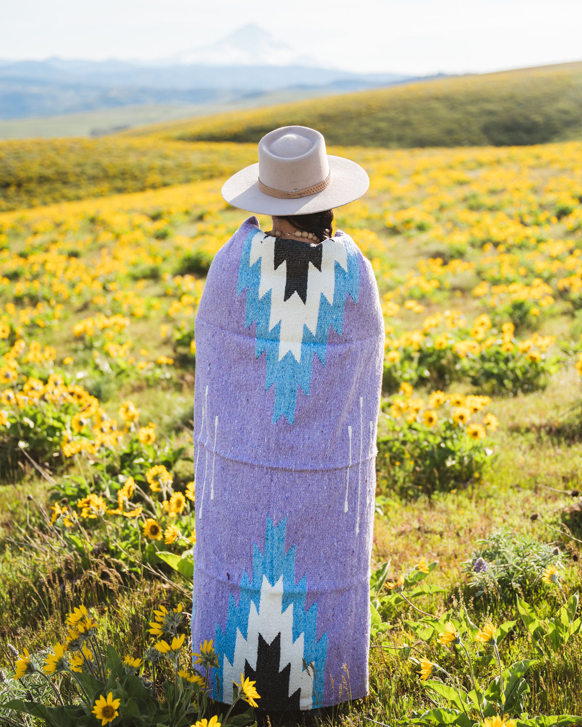 Person wrapped in a patterned blanket standing in a field of wildflowers