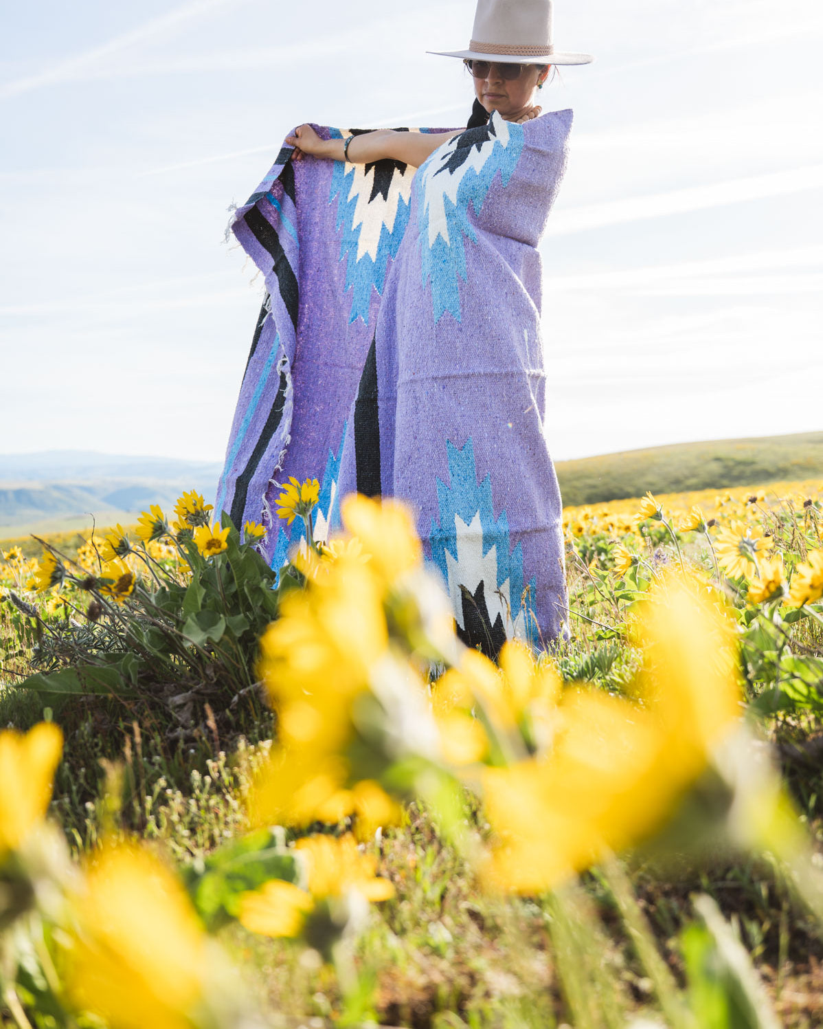 Person holding a colorful patterned blanket in a field of yellow flowers