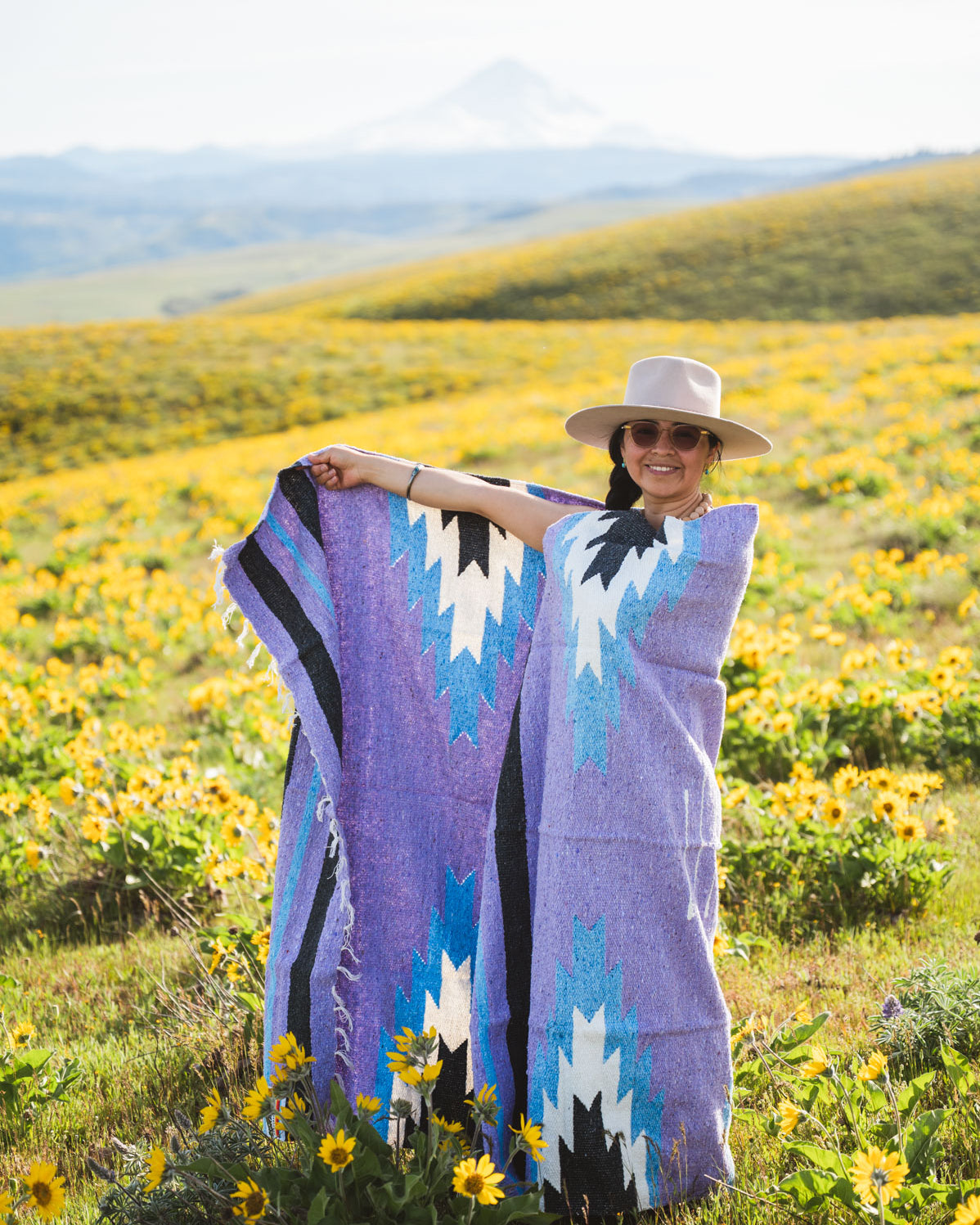 Woman holding a colorful patterned blanket in a field of wildflowers with mountains in the background