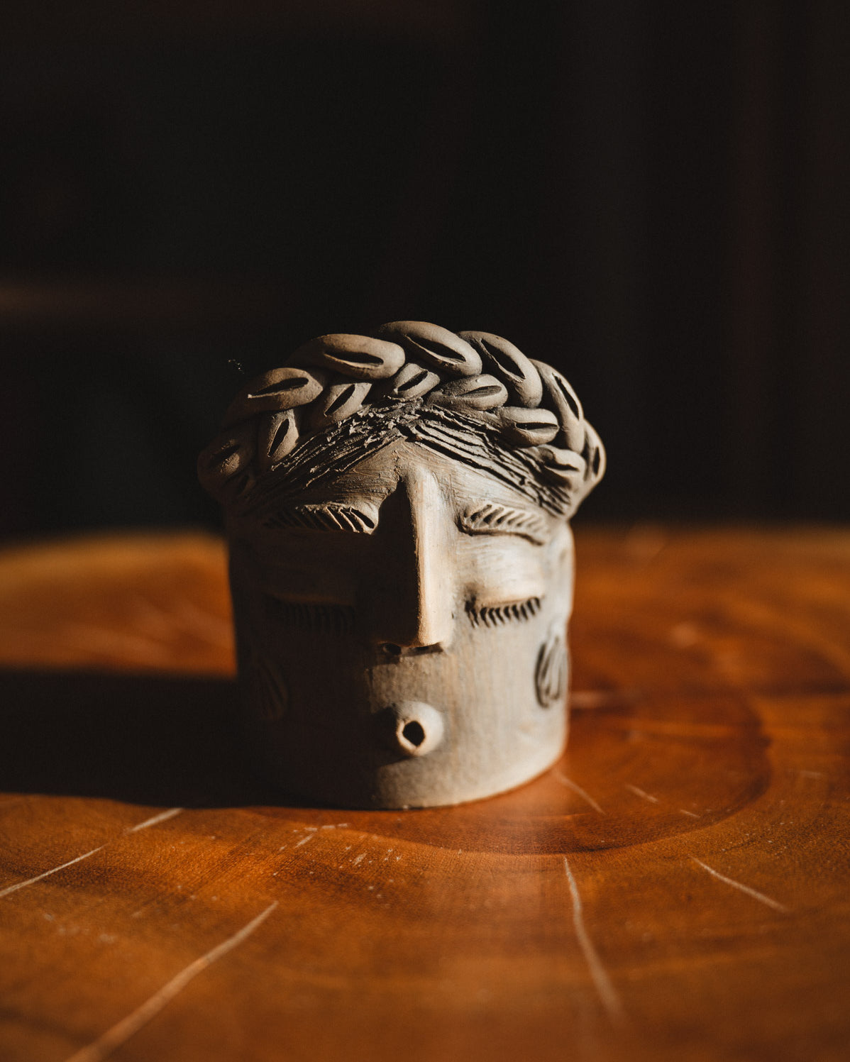 Ceramic face sculpture on a wooden surface with a dark background