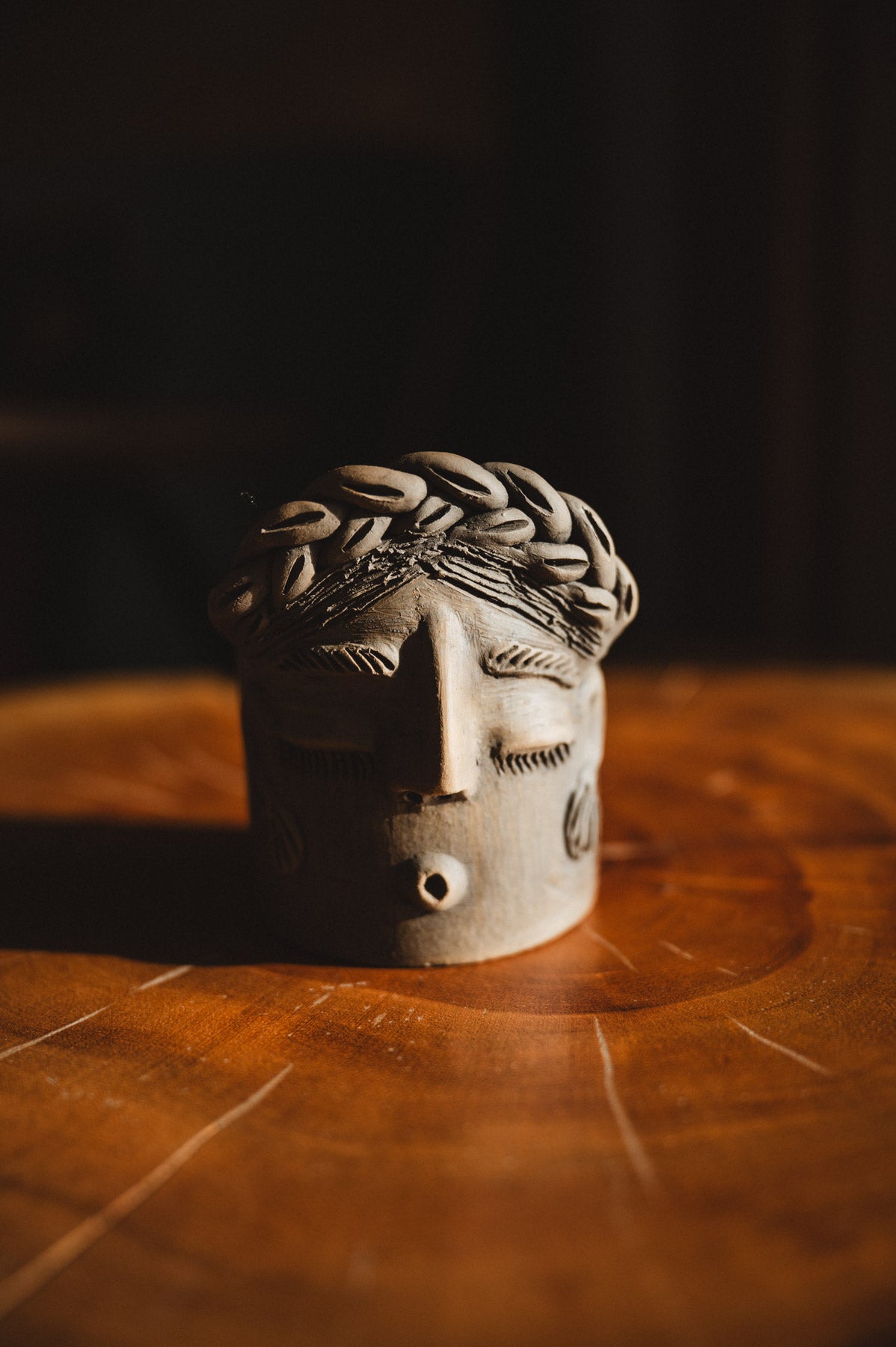 Ceramic face sculpture on a wooden surface with a dark background