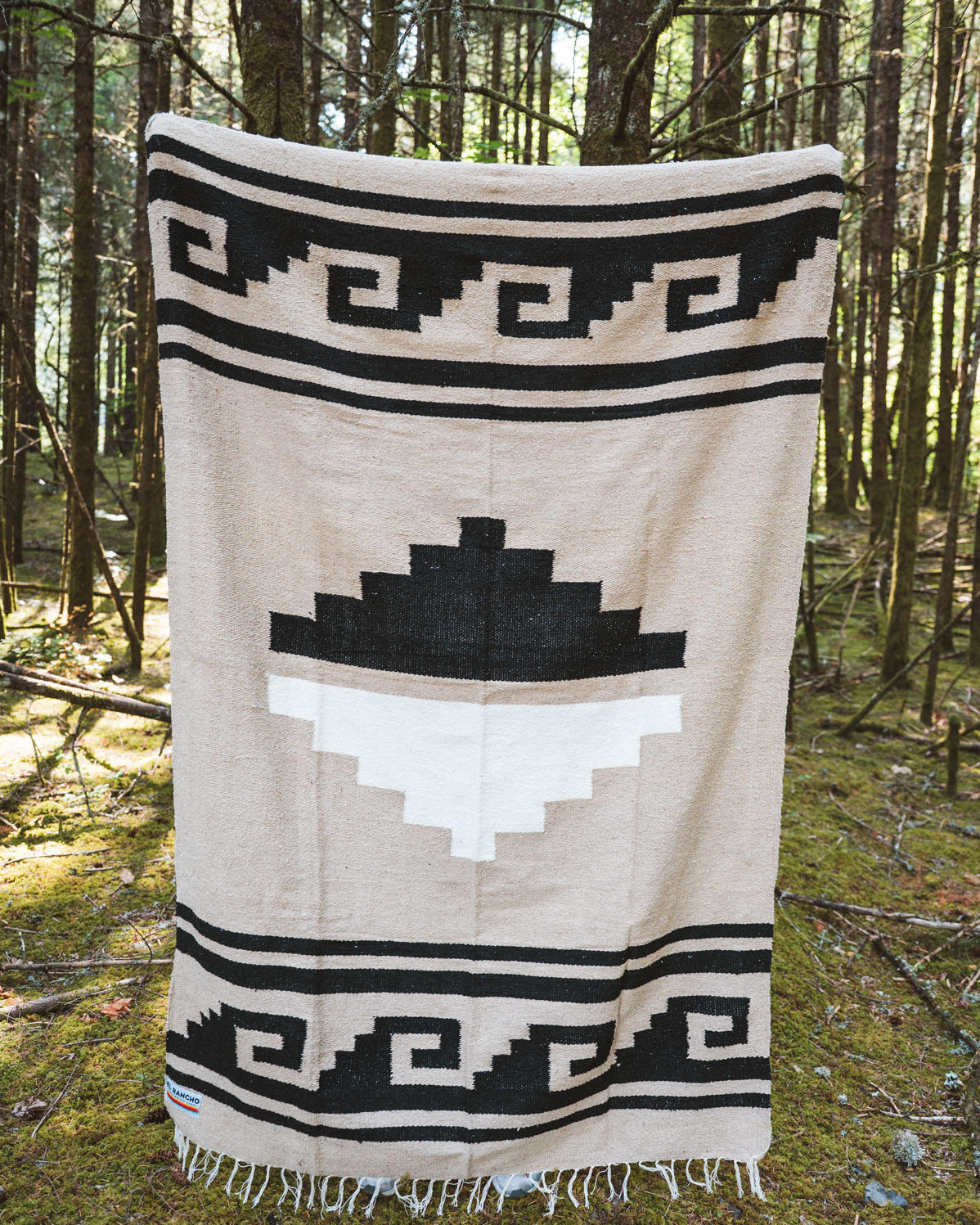 Black and beige greca patterned handwoven mexican blanket in a forest background