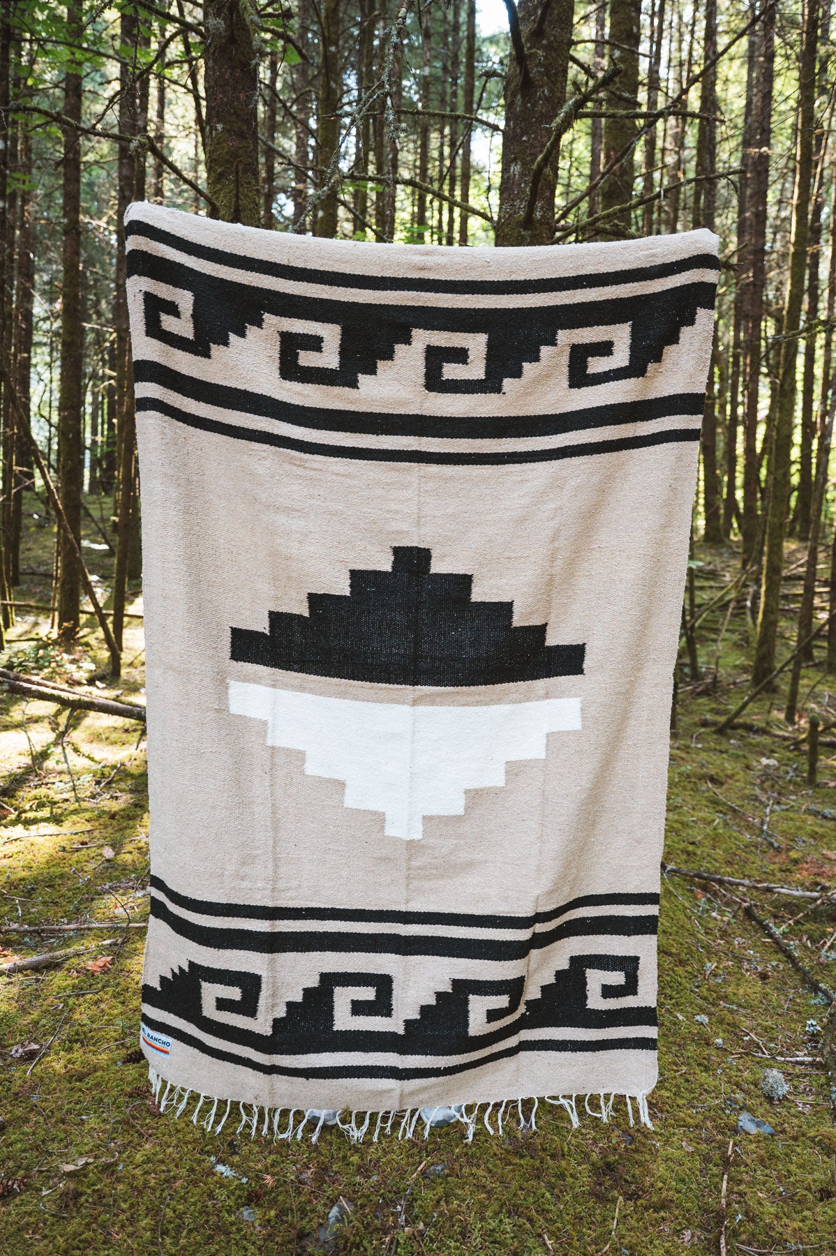 Black and beige greca patterned handwoven mexican blanket in a forest background