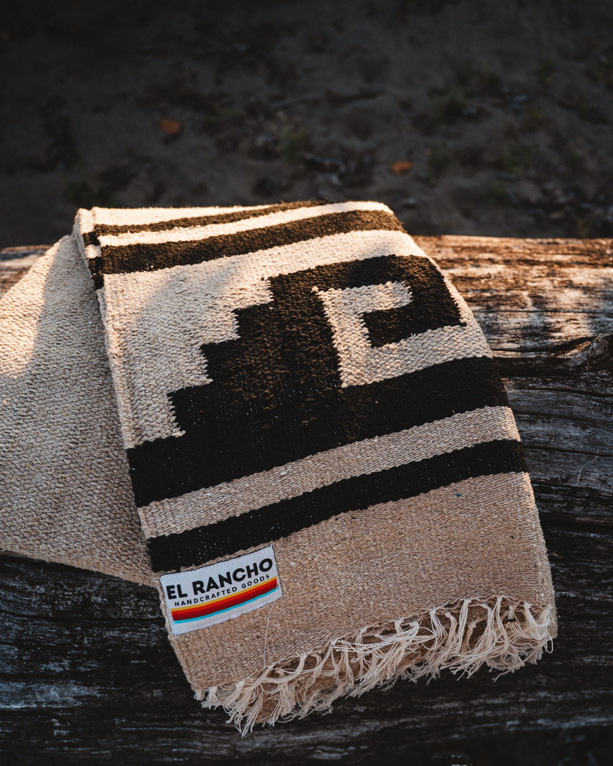 Beige and brown patterned blanket with 'El Rancho' logo on a wooden surface