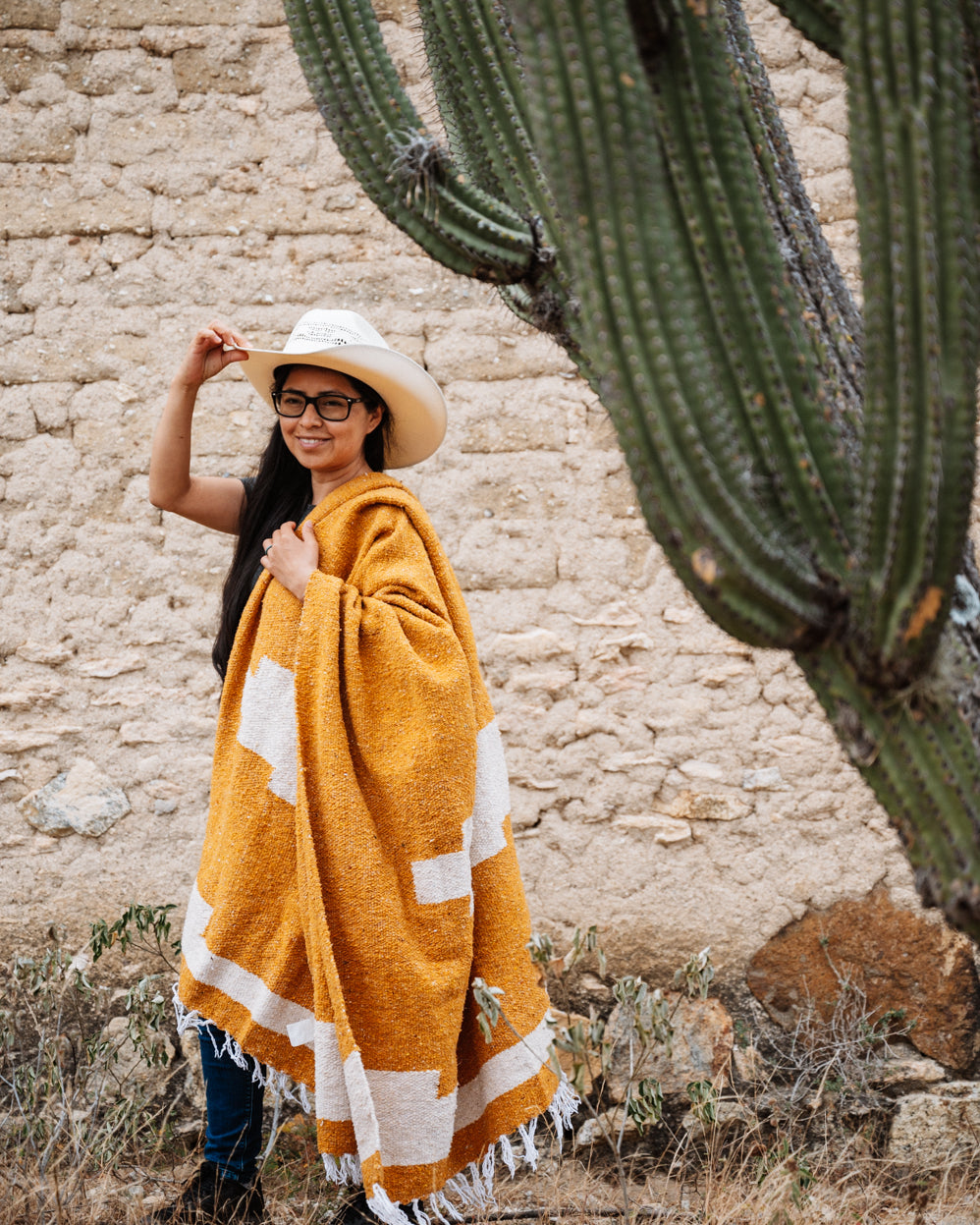 Girl wrapped in orange blanket in front of a cactus in Oaxaca