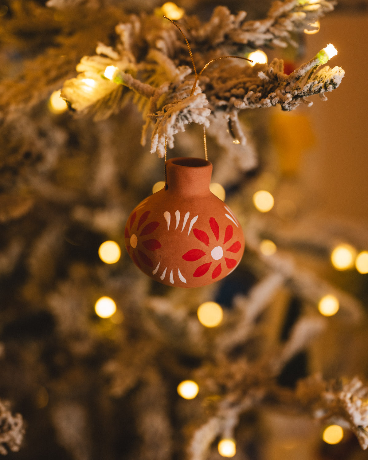 Decorative ornament with floral patterns hanging on a Christmas tree with lights.