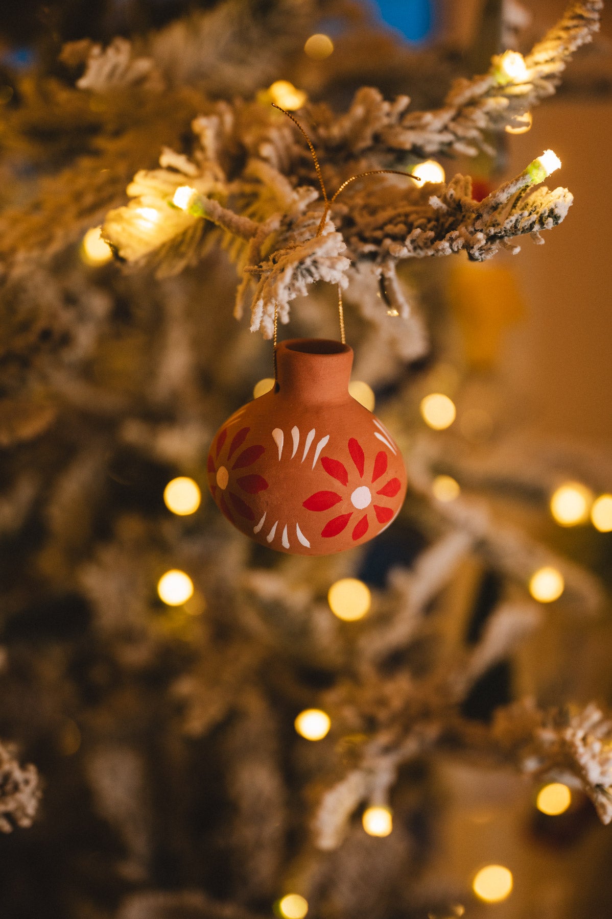 Decorative ornament with floral patterns hanging on a Christmas tree with lights.