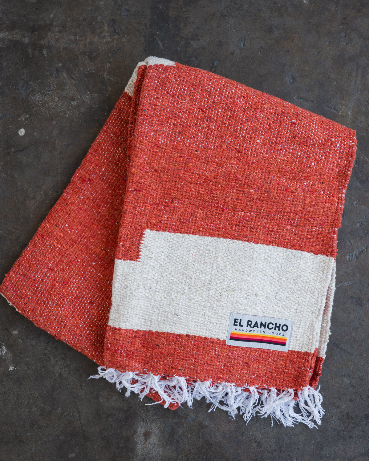 Red handwoven throw blanket folded laying on concrete floor