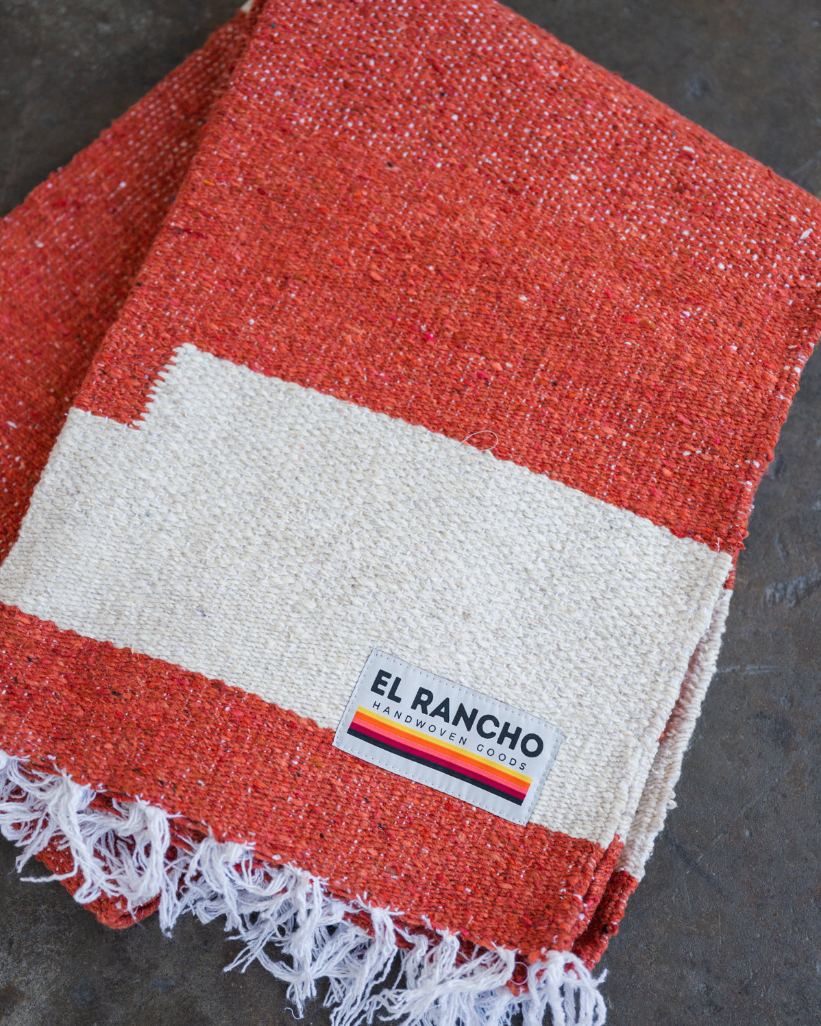 Red handwoven throw blanket folded laying on concrete floor