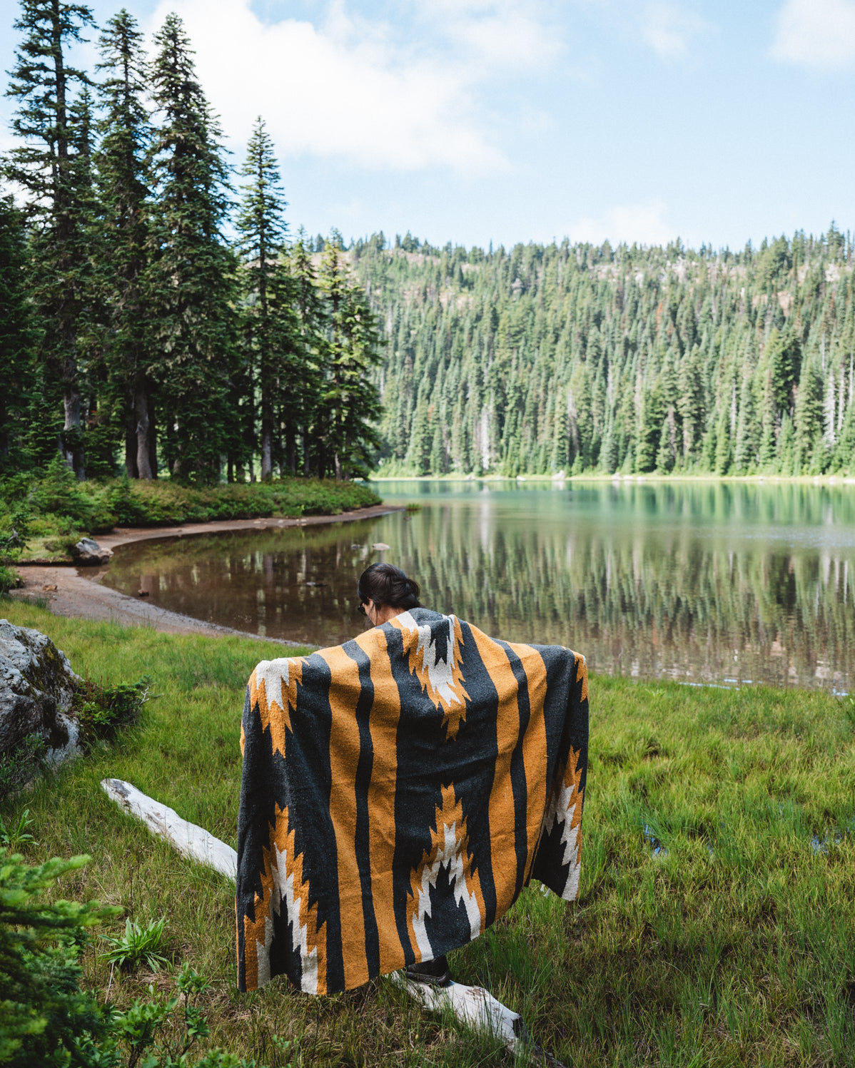 Girl wearing black and yellow zapotec handwoven mexican blanket in front of alpine lake