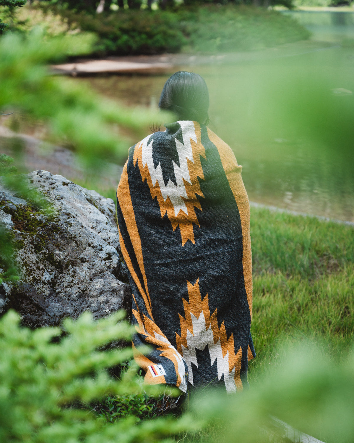 Girl wearing black and yellow zapotec handwoven mexican blanket in front of alpine lake