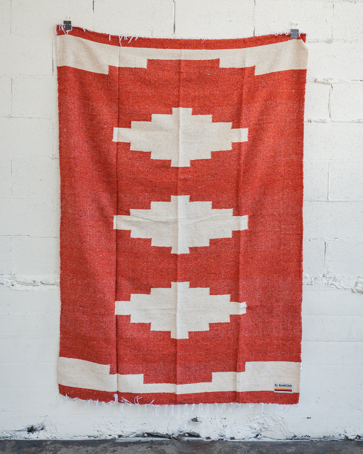Red diamond handwoven Mexican Blanket hanging on white brick wall