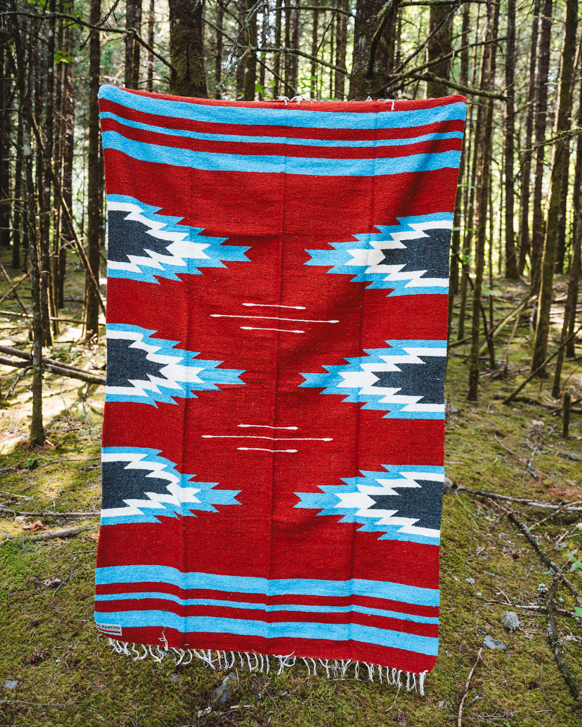 Red and blue relampago patterned handwoven mexican blanket in a forest background