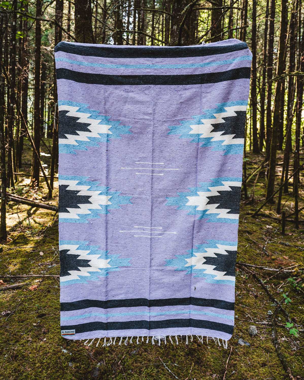 Lavender and blue relampago patterned handwoven mexican blanket in a forest background