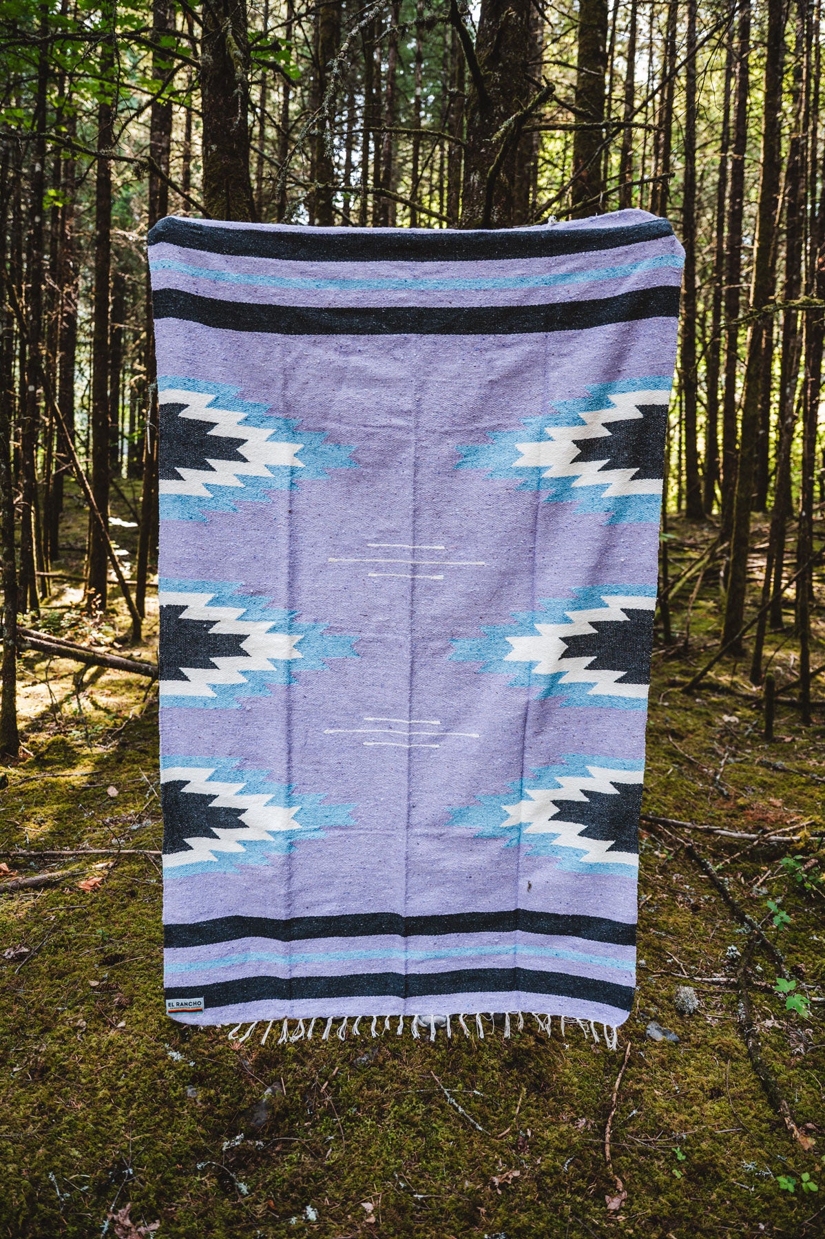 Lavender and blue relampago patterned handwoven mexican blanket in a forest background