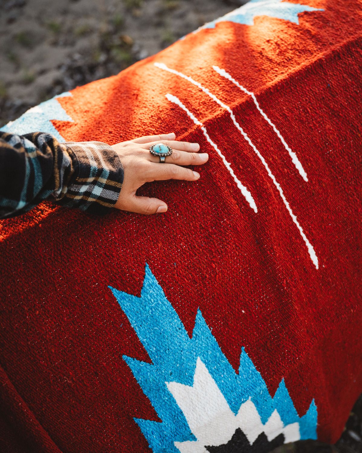 Hand with a ring on a red patterned fabric with blue and white designs.