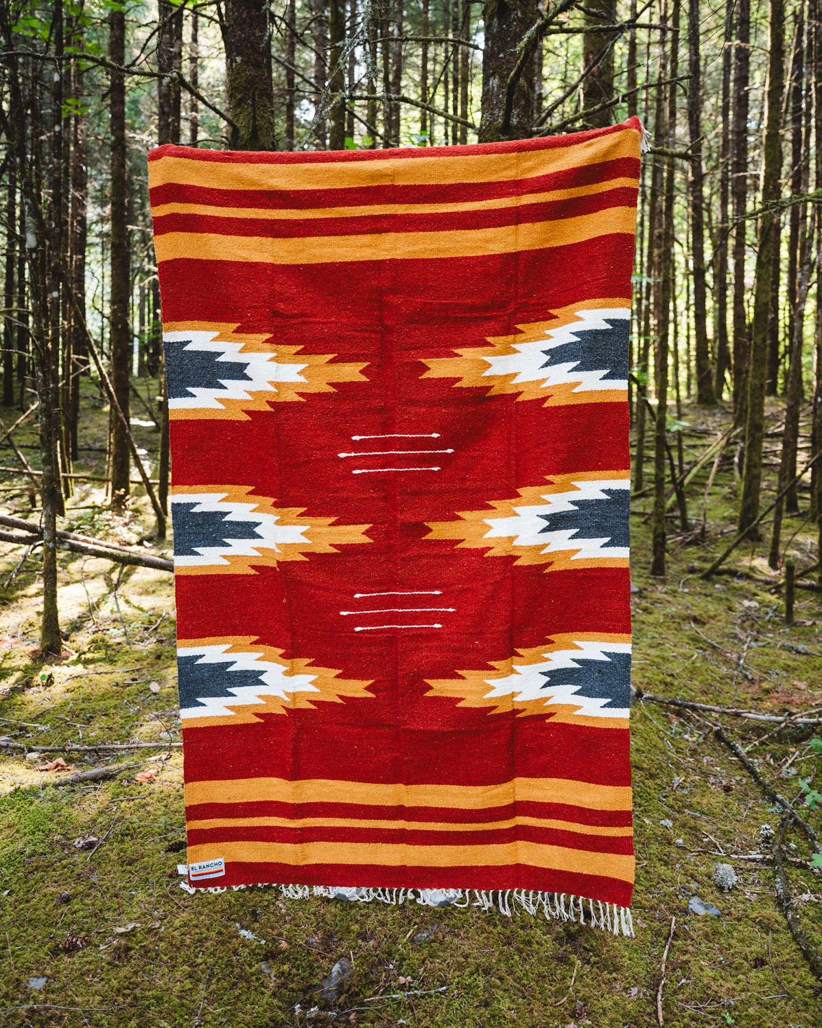 Red and yellow relampago patterned handwoven mexican blanket in a forest background