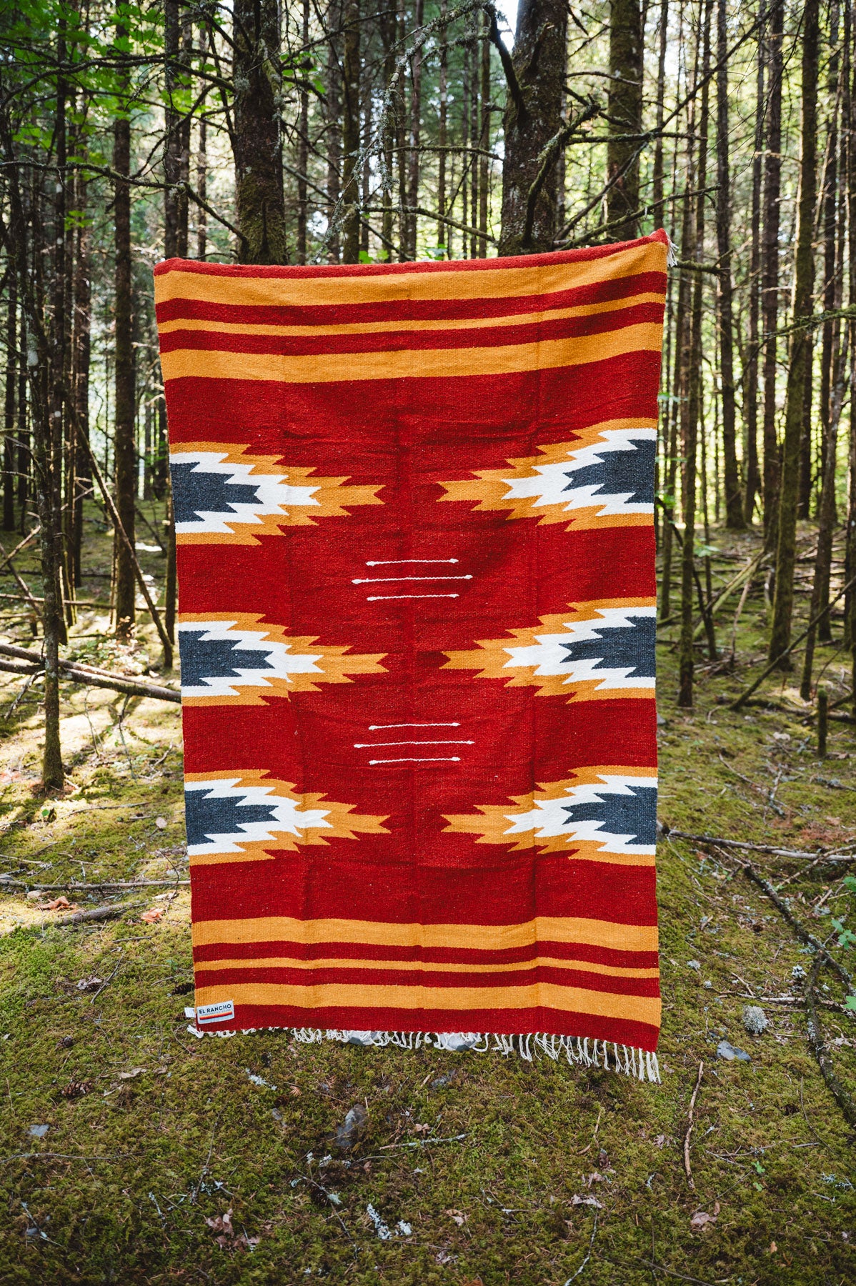 Red and yellow relampago patterned handwoven mexican blanket in a forest background