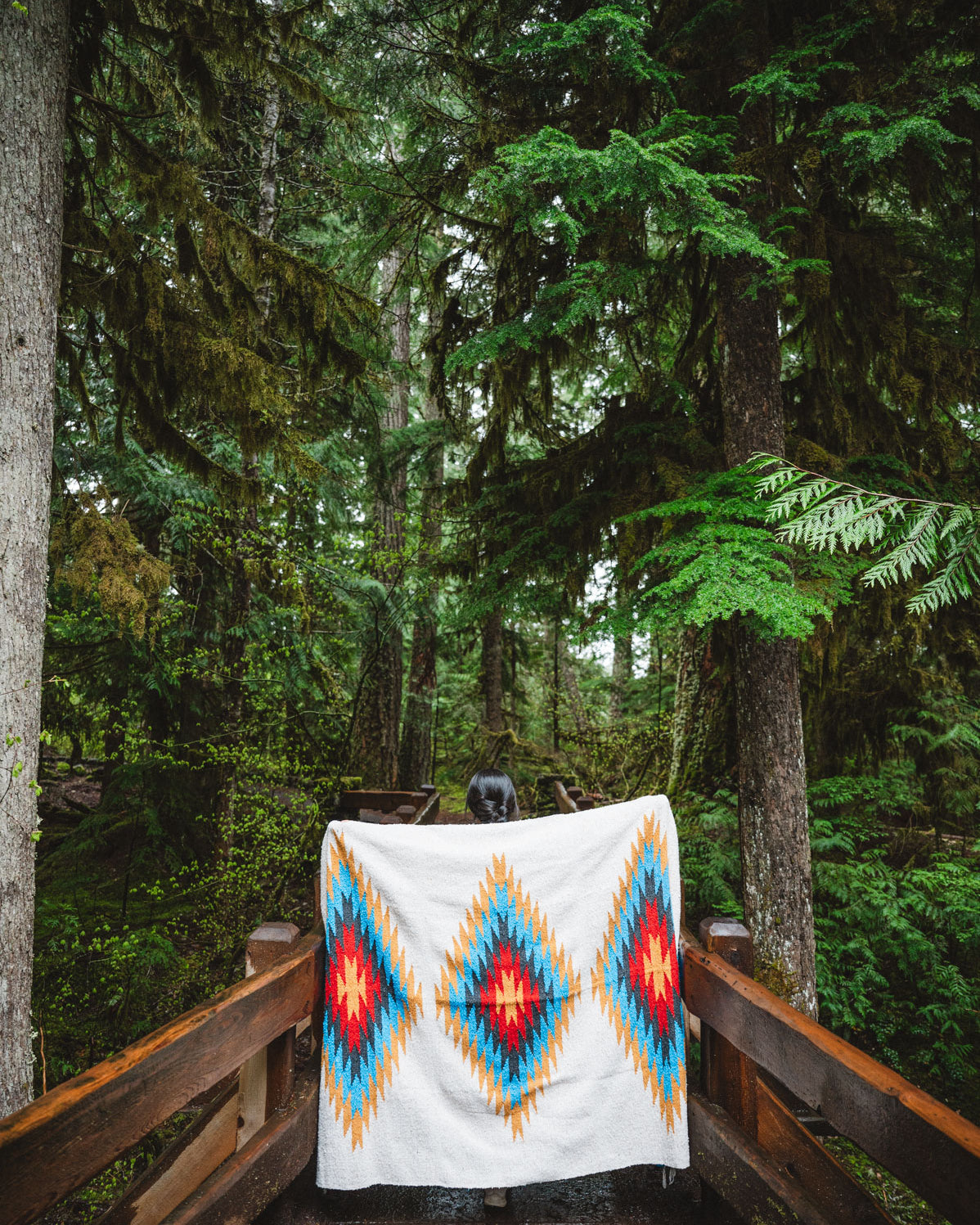 Woman wearing a Handwoven Mexican Blanket in front of Sahalie Falls Oregon in the Mckenzie River Corridor walking bridge