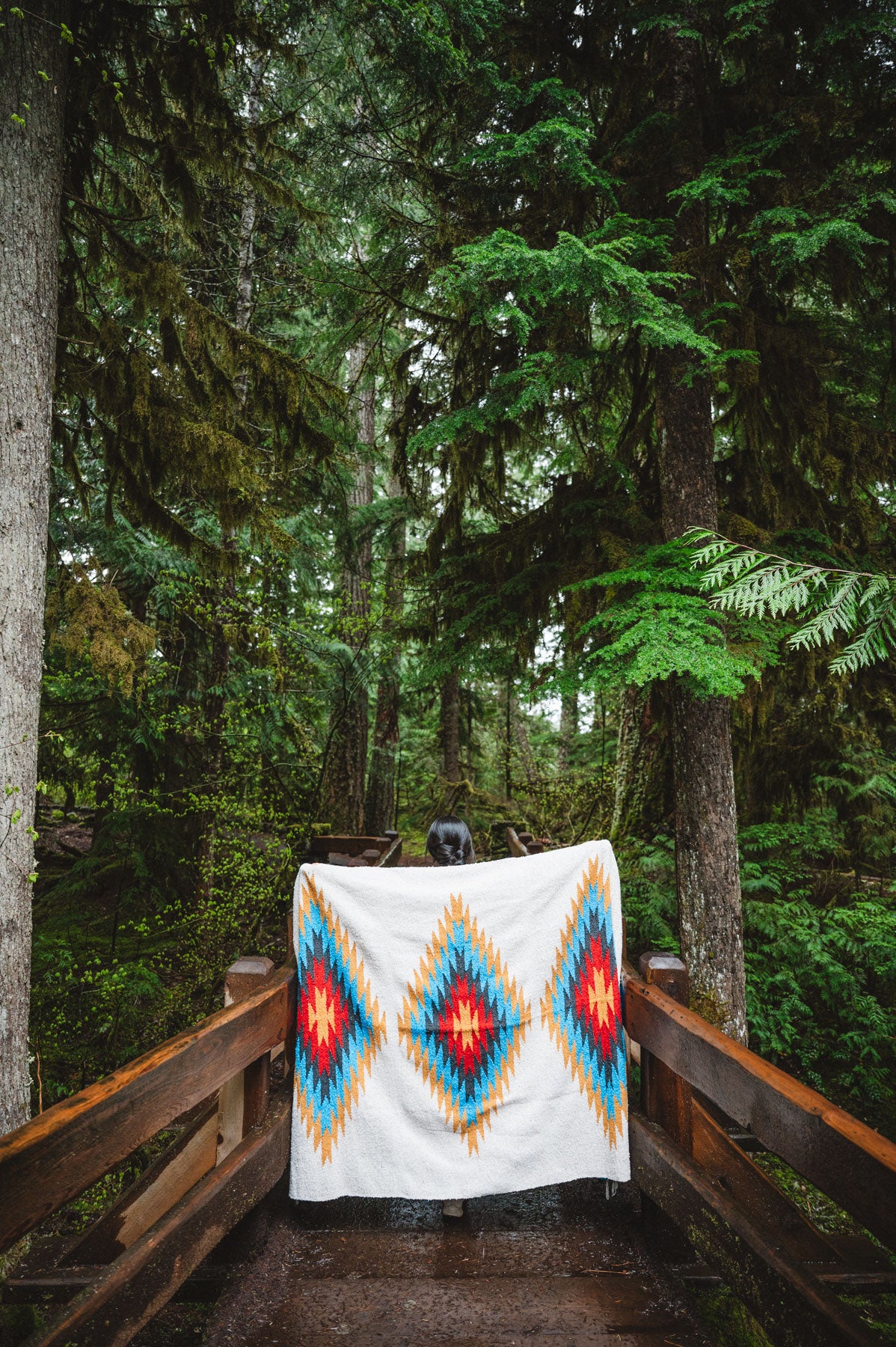 Woman wearing a Handwoven Mexican Blanket in front of Sahalie Falls Oregon in the Mckenzie River Corridor walking bridge