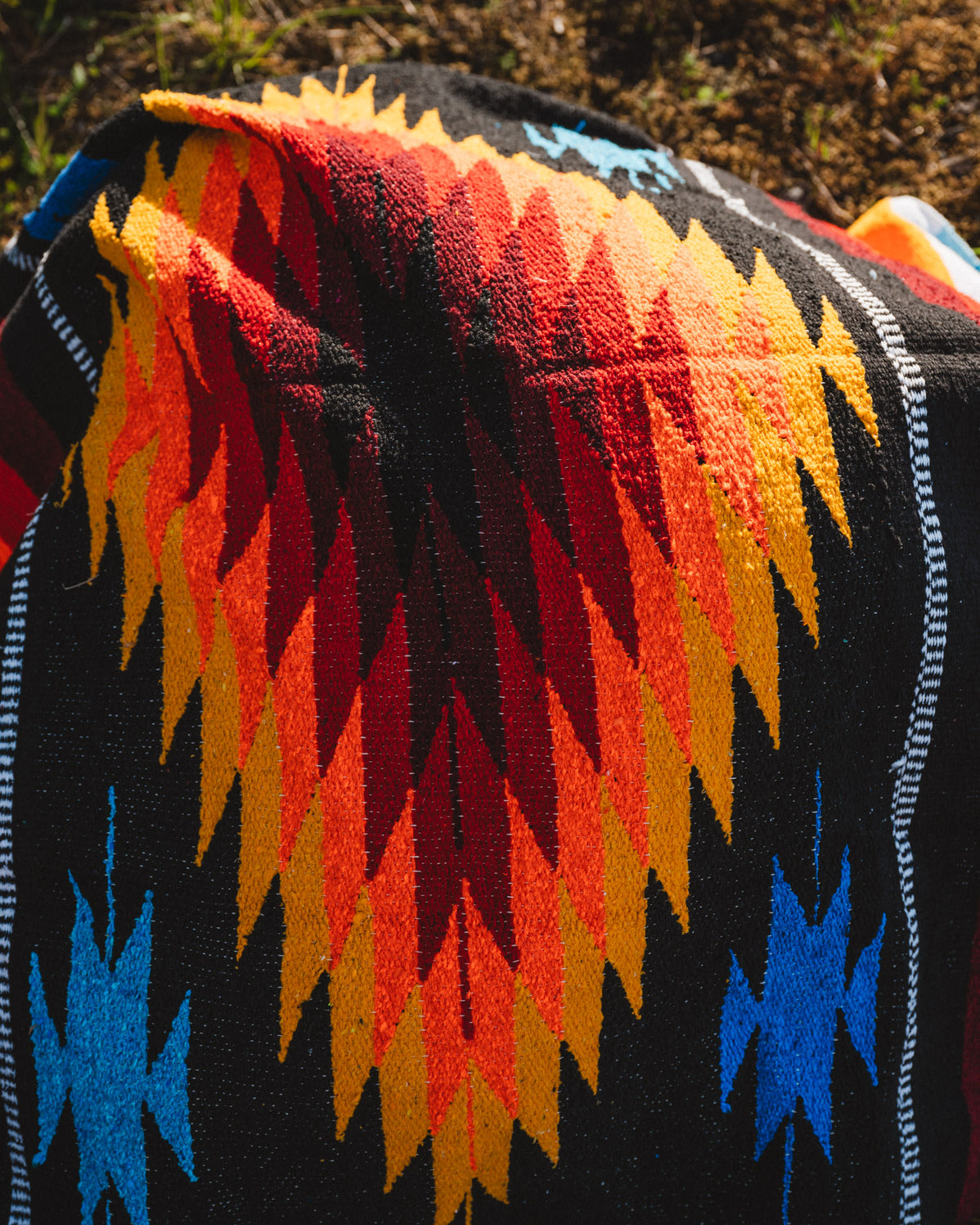 Mulitcolored handwoven mexican diamond blanket laying on the ground