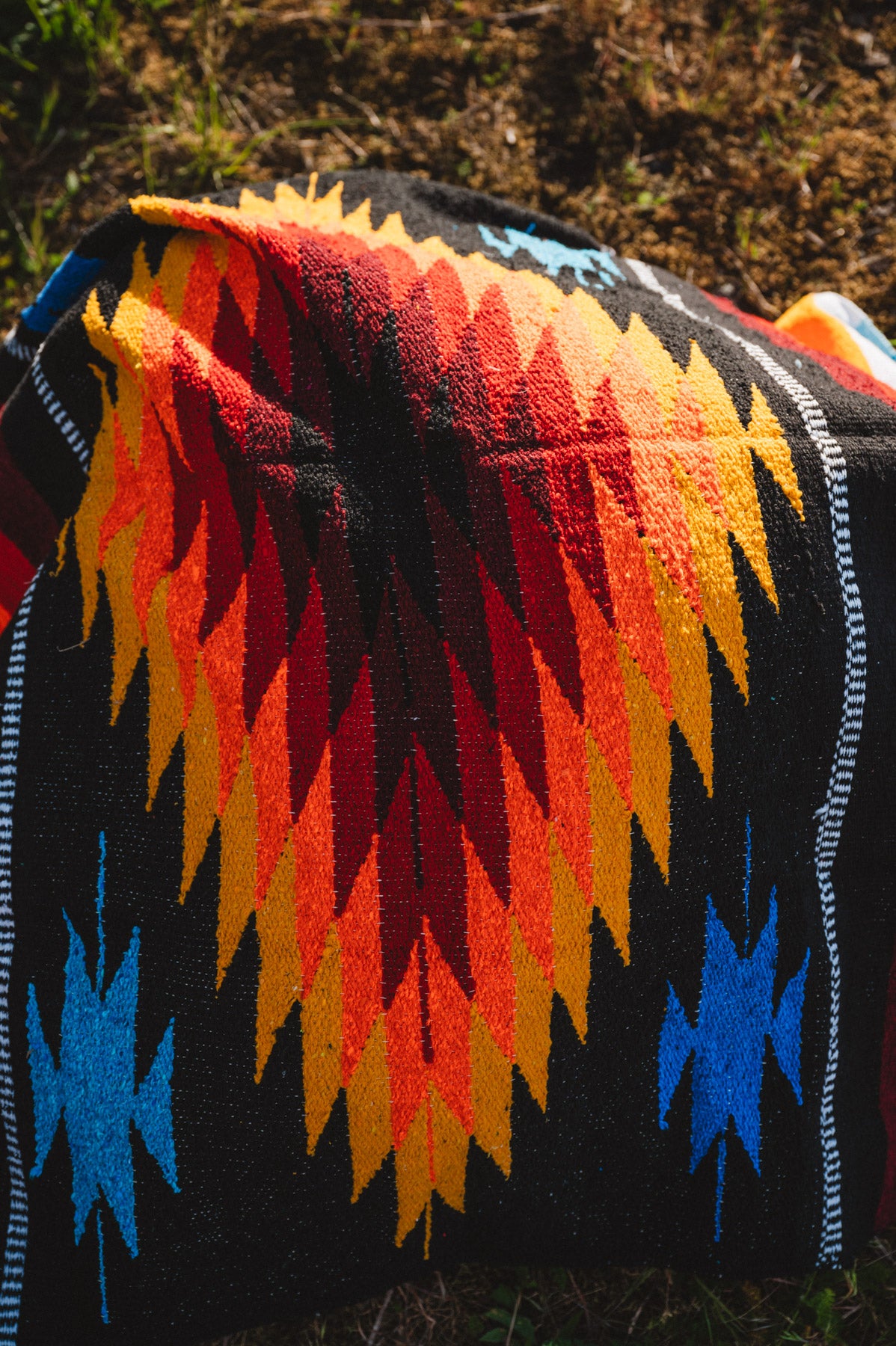 Mulitcolored handwoven mexican diamond blanket laying on the ground