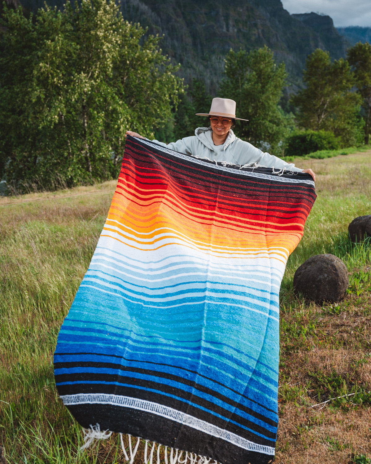 Mexican woman holding multicolored handwoven mexican blanket with striped saltillo design