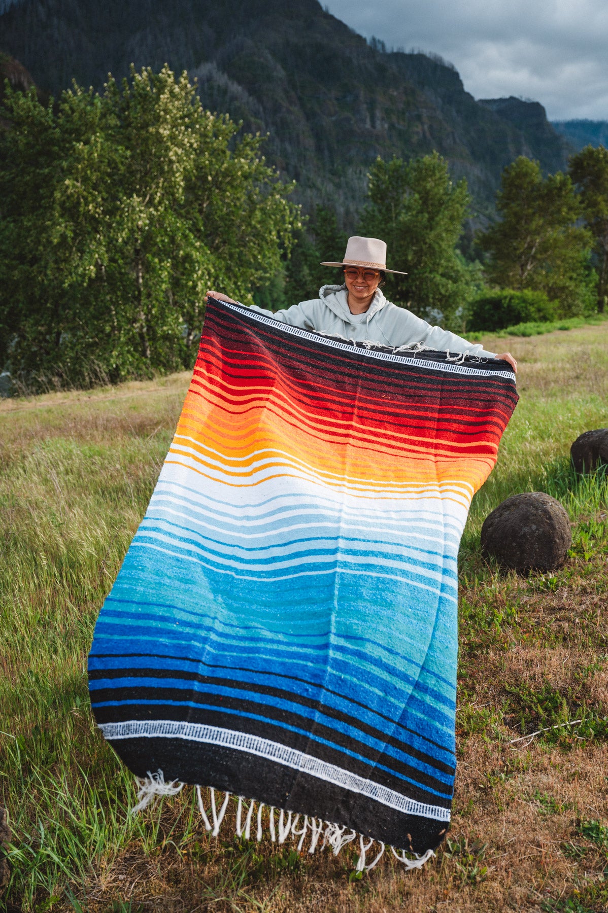 Mexican woman holding multicolored handwoven mexican blanket with striped saltillo design