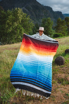 Mexican woman holding multicolored handwoven mexican blanket with striped saltillo design