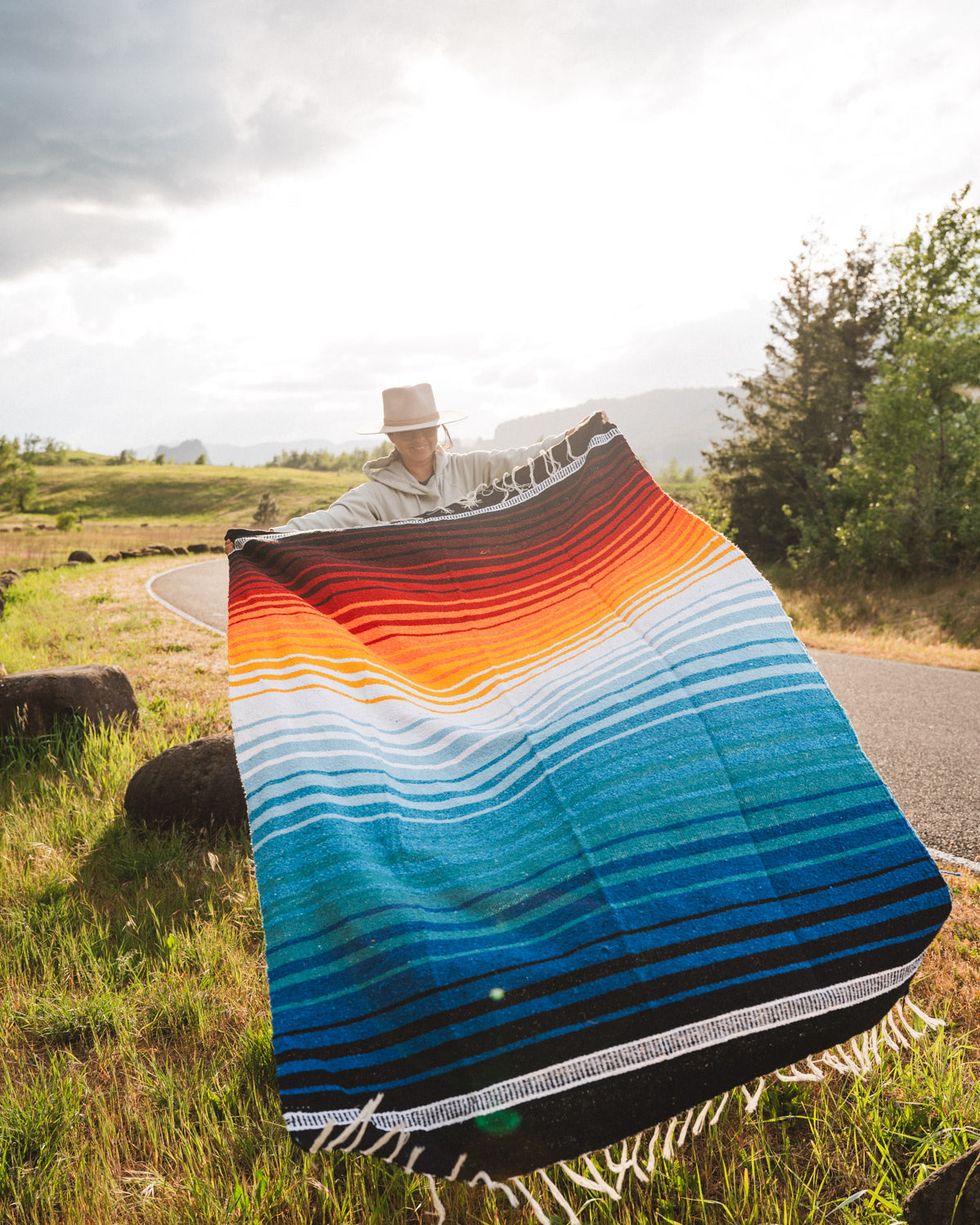 Mexican woman holding multicolored handwoven mexican blanket with striped saltillo design