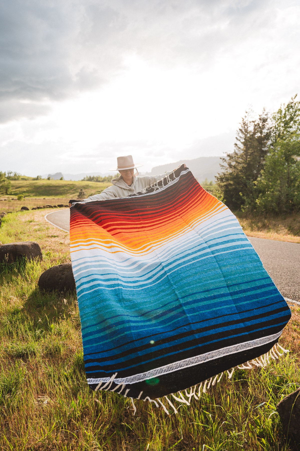 Mexican woman holding multicolored handwoven mexican blanket with striped saltillo design