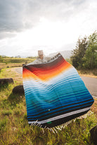 Mexican woman holding multicolored handwoven mexican blanket with striped saltillo design