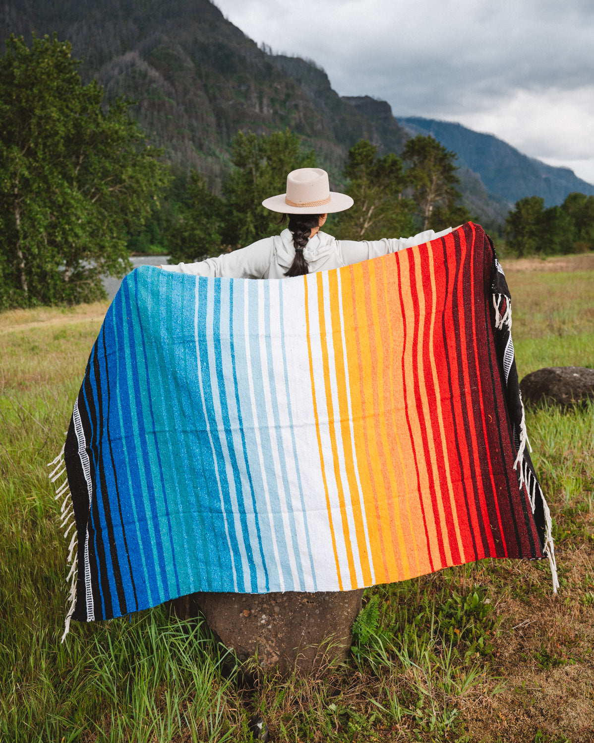 Mexican woman holding multicolored handwoven mexican blanket with striped saltillo design