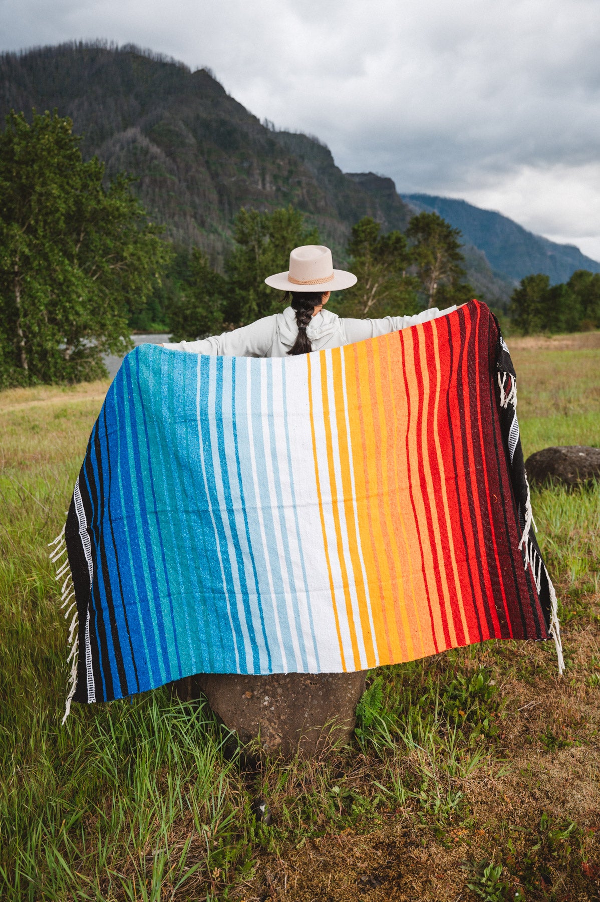 Mexican woman holding multicolored handwoven mexican blanket with striped saltillo design