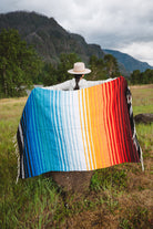 Mexican woman holding multicolored handwoven mexican blanket with striped saltillo design